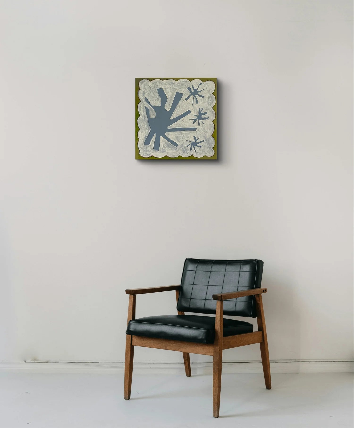 Black armchair with wooden frame against a white wall with a framed abstract artwork. "Counting My Lucky Stars original acrylic painting by Marley Alvarez"