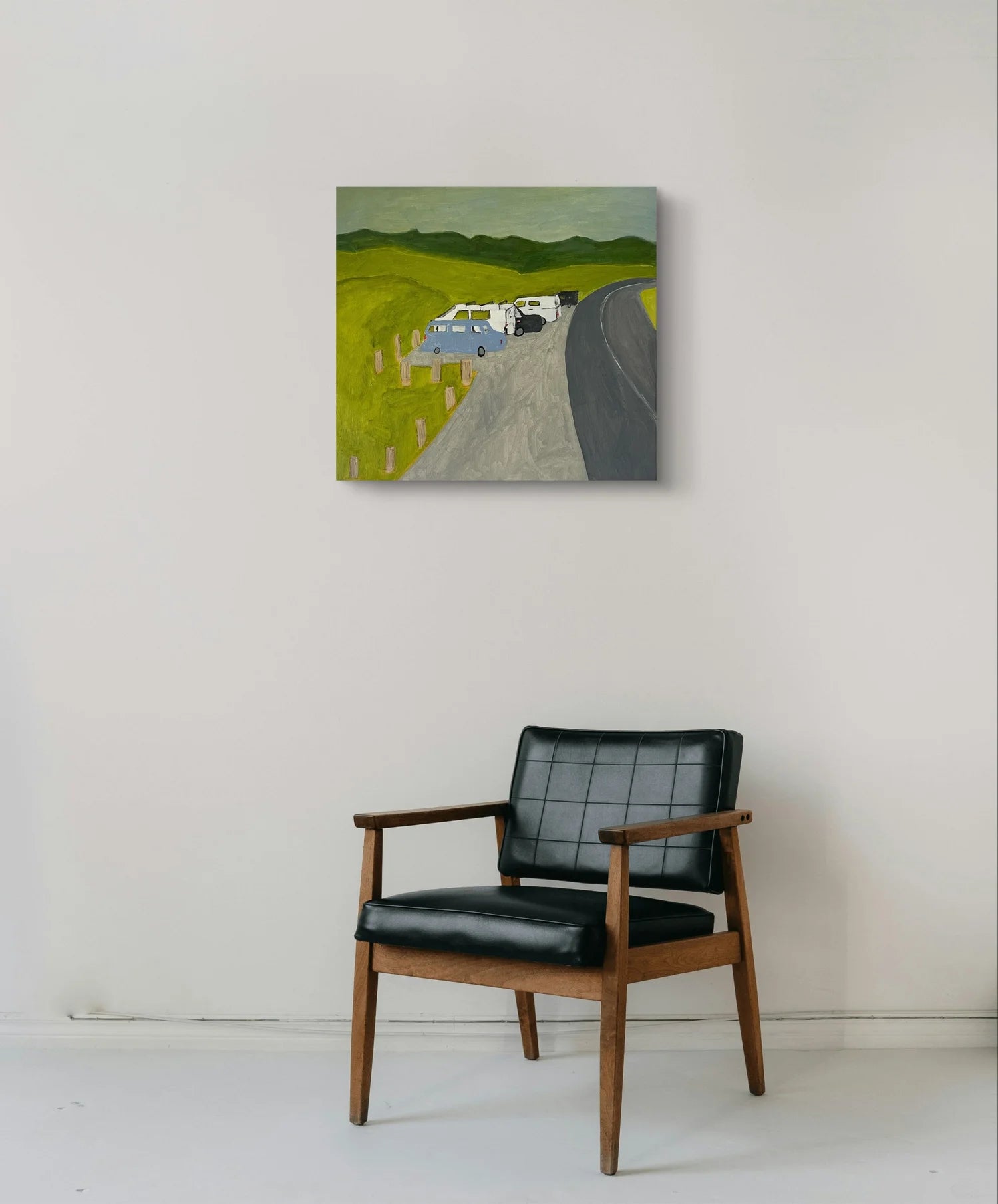 Black armchair in front of a painting of a road with a car on a white wall.