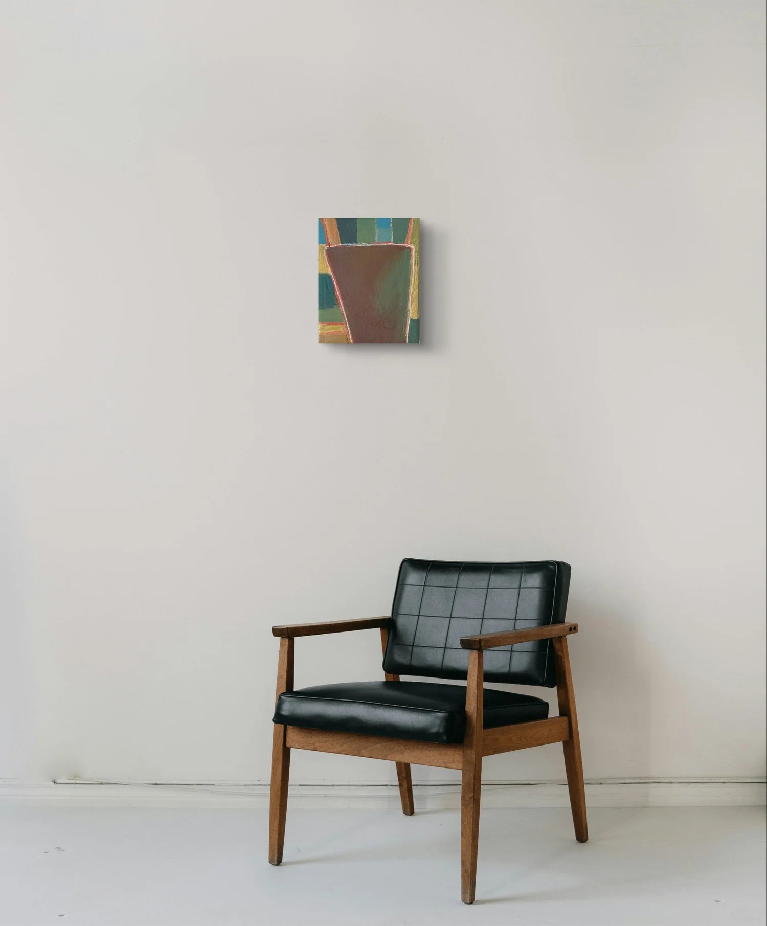 Black leather armchair with wooden frame against a white wall with a abstract painting 'Tunnel To Tomorrow' by Marley Alvarez.
